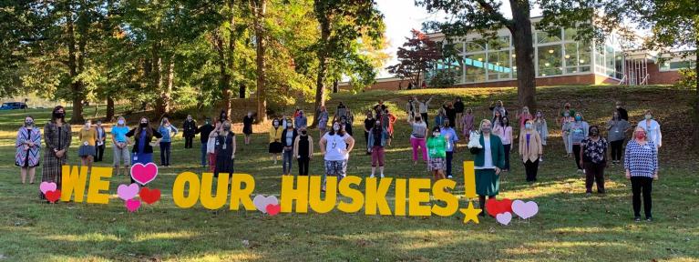 We Love Our Huskies sign outside school with staff socially distanced