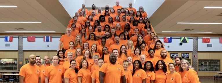 Group photo of Heritage High School staff in matching shirts standing on stairs