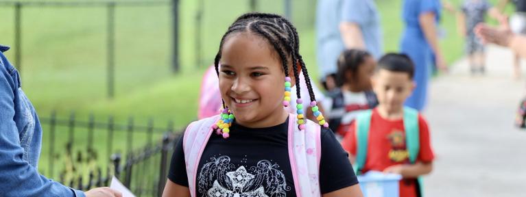Girl with backpack smiling walking into school