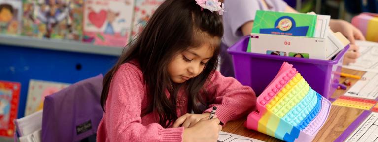 Girl writing at desk with a colorful pencil pouch and books in the background