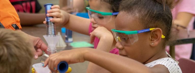 Students wearing goggles pouring liquid in test tubes