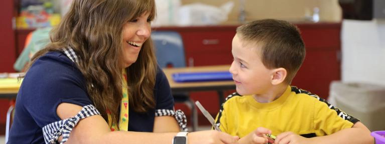 Staff member and student sitting at table in classroom looking at each other smiling