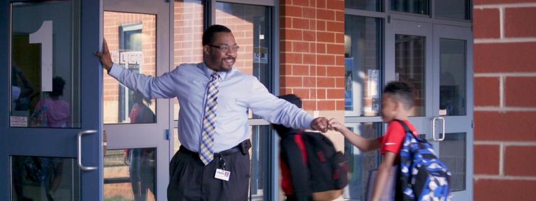 Principal greeting students while holding door